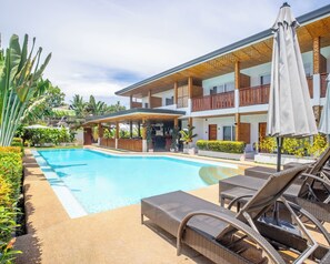 A poolside area with lounge chairs and a bar, surrounded by a building with balconies and a covered patio. - Yellow Mango Resort Bohol (Panglao)