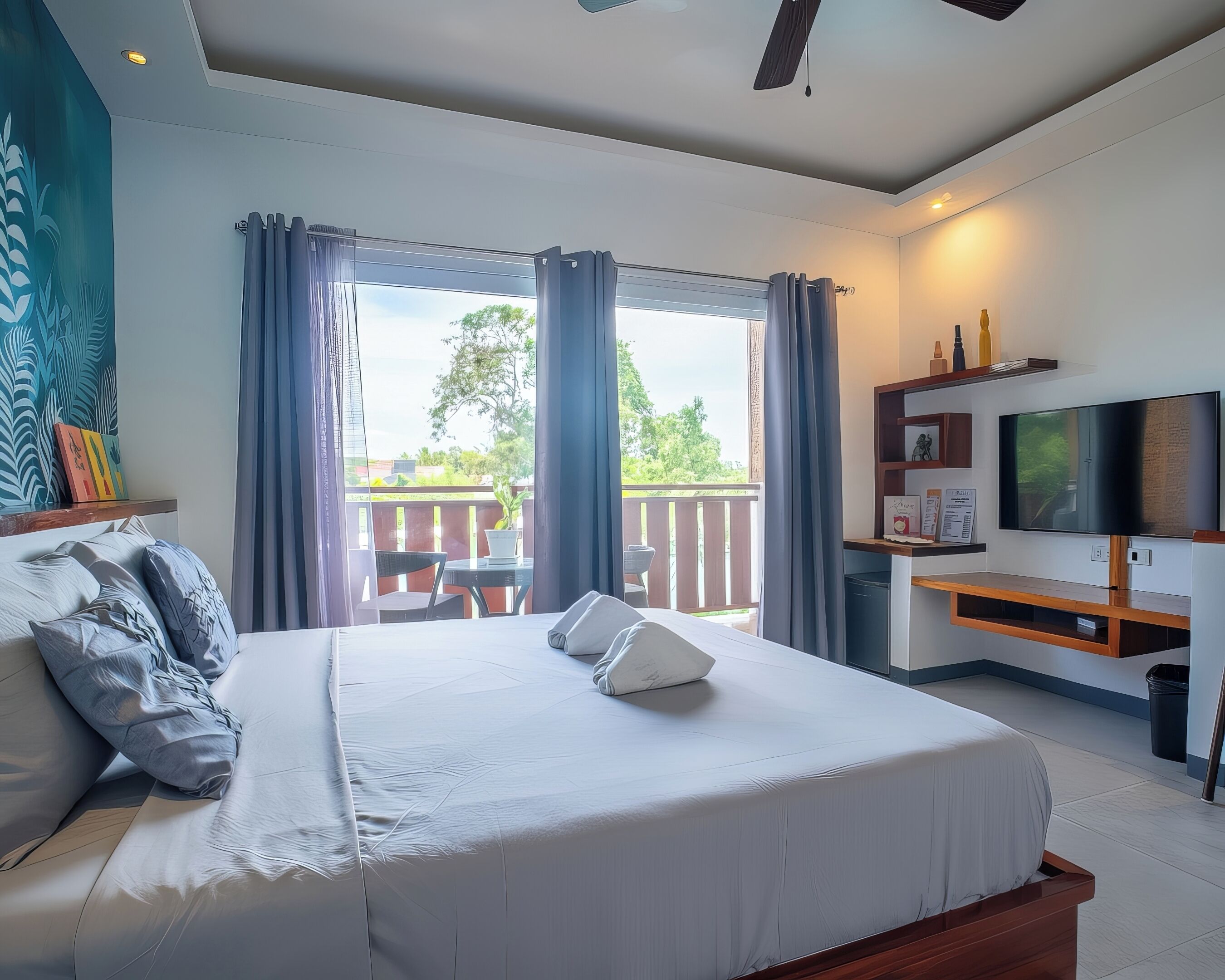 Quarto de hotel moderno com uma cama grande, televisão, escrivaninha e varanda com vista para o exterior.
