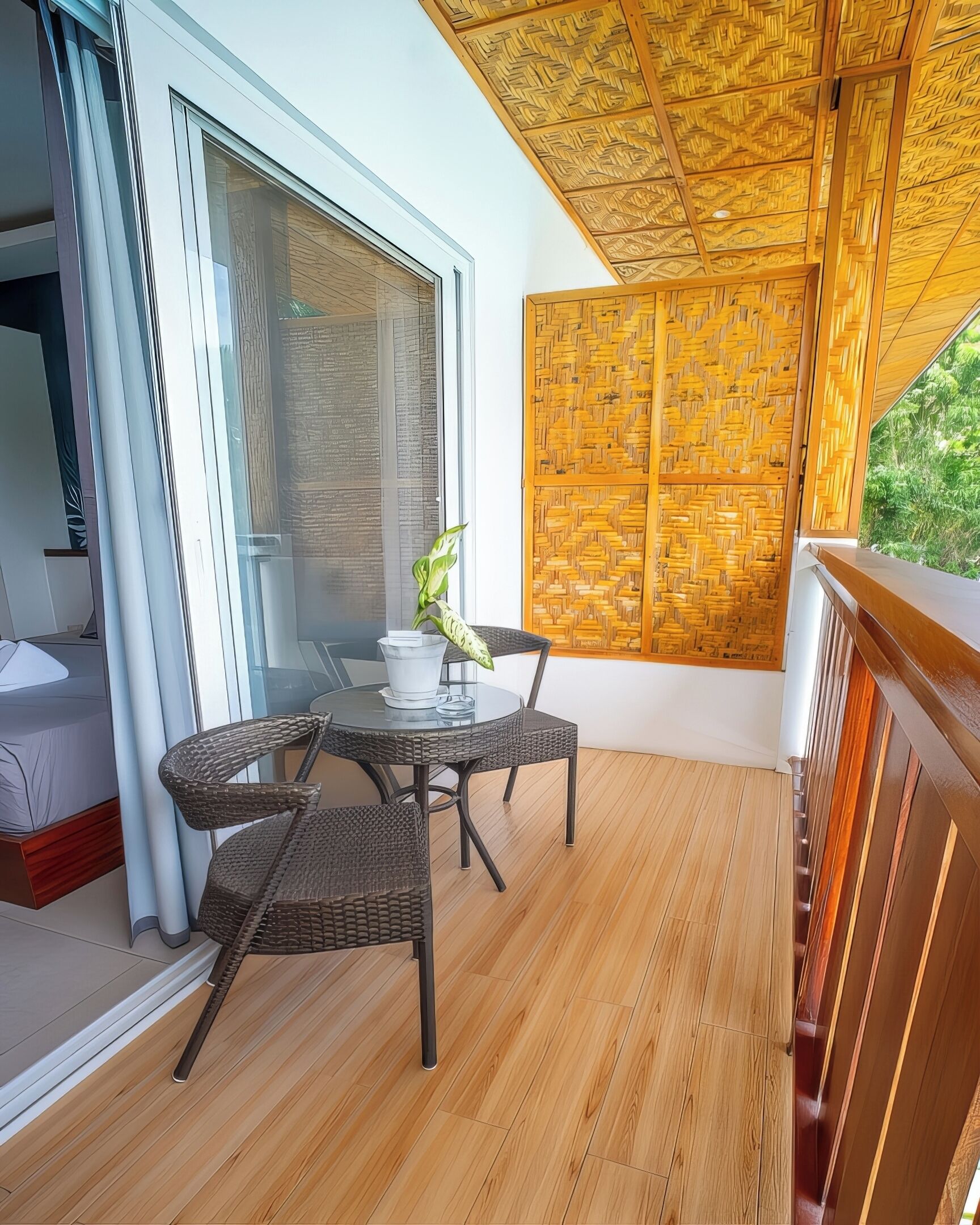 A balcony with a wooden floor, a glass table with chairs, and a view of greenery.