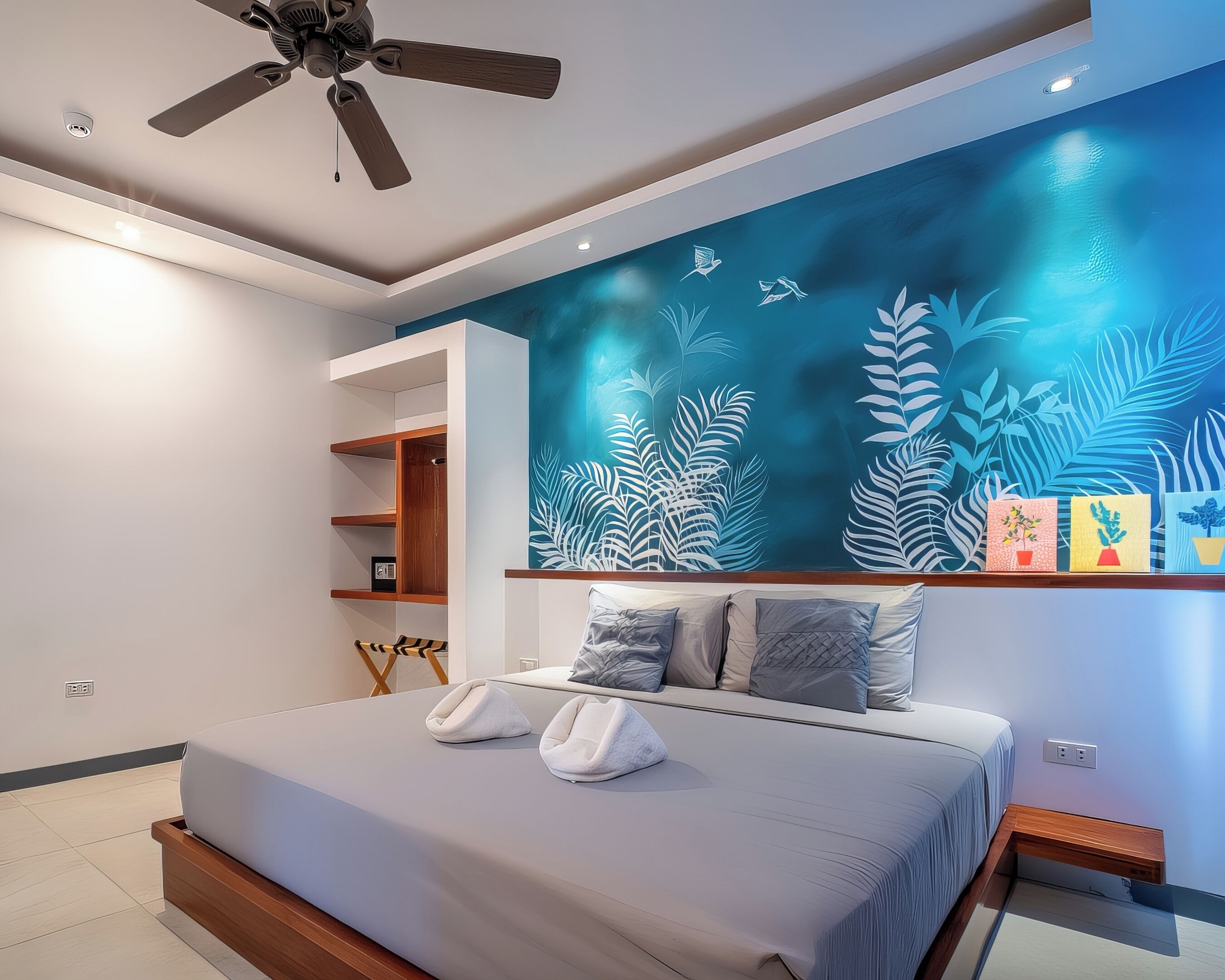 A modern bedroom with a bed, a ceiling fan, and a wall with a tropical leaf design.