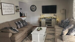 Ein Wohnzimmer mit braunem Sofa, weißem Couchtisch, Kamin und einem an der Wand befestigten Fernseher.