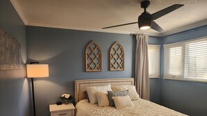 Ein Schlafzimmer mit einem Bett, einem Nachttisch, einer Lampe, einem Deckenventilator und zwei Wanddekorationen.