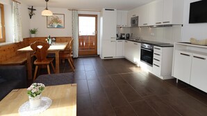 A modern kitchen with white cabinets, a built-in oven, and a microwave. There's a dining area with a wooden table and chairs, and a small potted plant on the table. - Spacious apartment near the ski lift (Fendels)