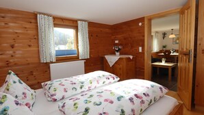 A wooden cabin bedroom with two beds, a small table, and a window with curtains. - Spacious apartment near the ski lift (Fendels)