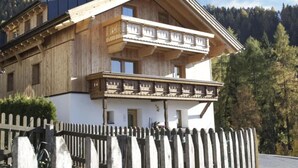 Un chalet en bois doté d’un balcon, entouré d’une clôture en bois et d’arbres.