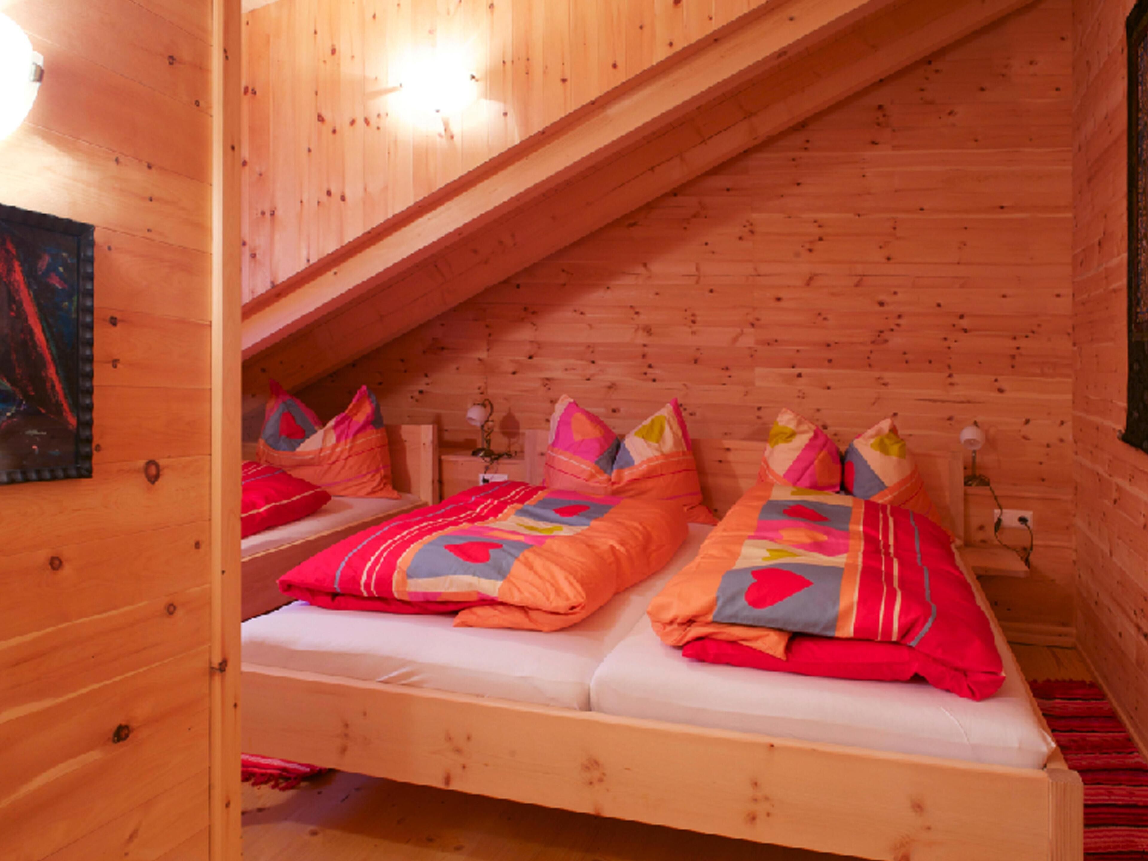 A cozy wooden cabin bedroom with two beds, a sloped ceiling, and a wall-mounted lamp.