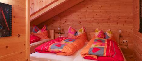 A cozy wooden cabin bedroom with two beds, a sloped ceiling, and a wall-mounted lamp.