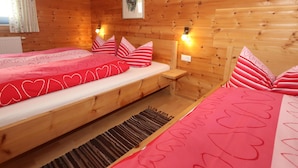 Une chambre rustique en bois avec deux lits, chacun agrémenté de draps à motifs de cœur, un tapis et un tableau au mur.