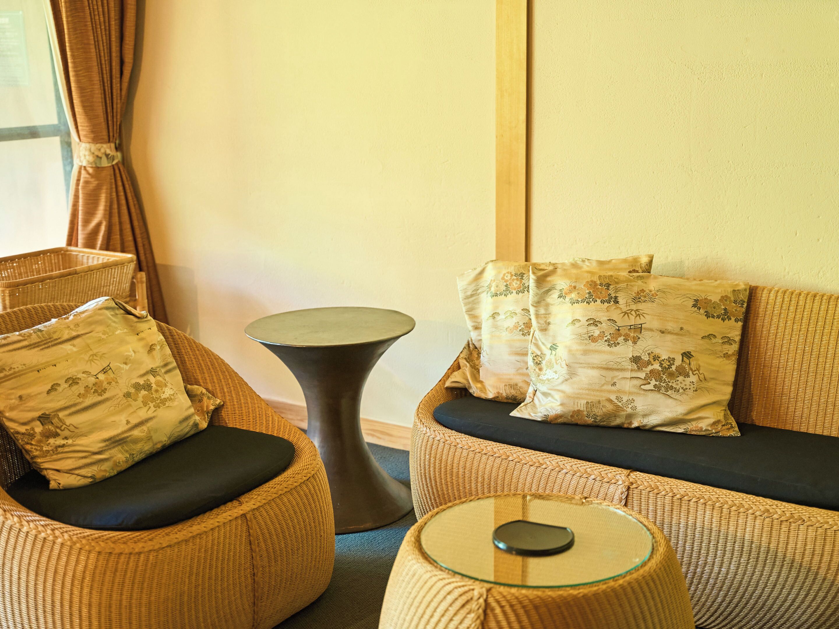 A wicker sofa with floral cushions, a small round table, and a wicker chair with a cushion.