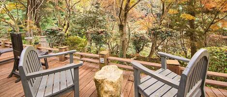 A wooden deck with benches and a stone stump, surrounded by trees with autumn foliage.