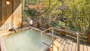 Una terraza de madera con aguas termales, rodeada de follaje denso.
