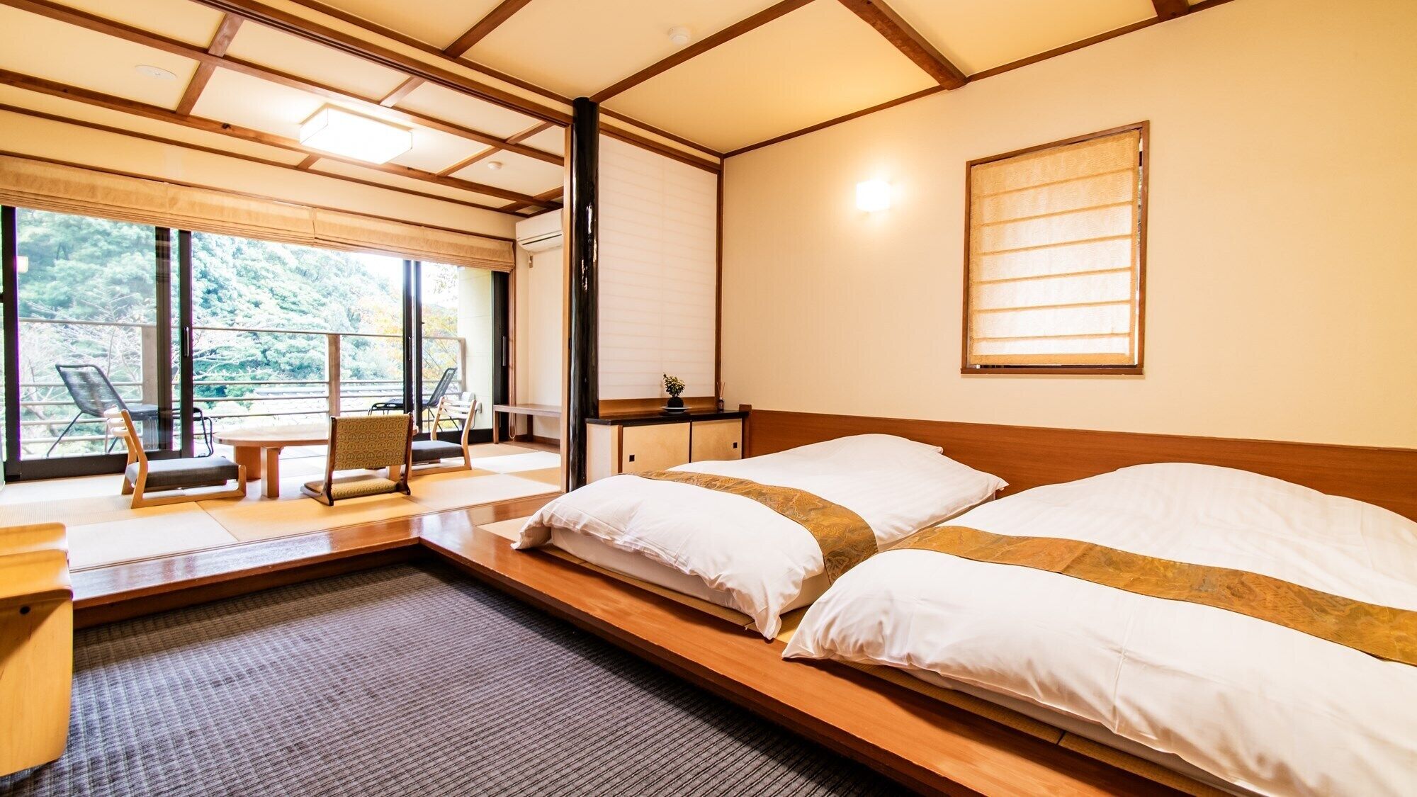 Une chambre avec un lit, une petite table, une chaise et une vue sur les arbres à travers de grandes fenêtres.