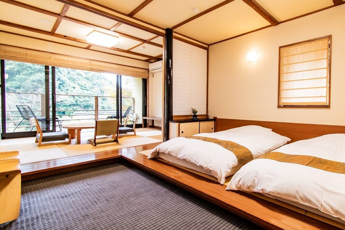 Une chambre avec un lit, une petite table, une chaise et une vue sur les arbres à travers de grandes fenêtres.