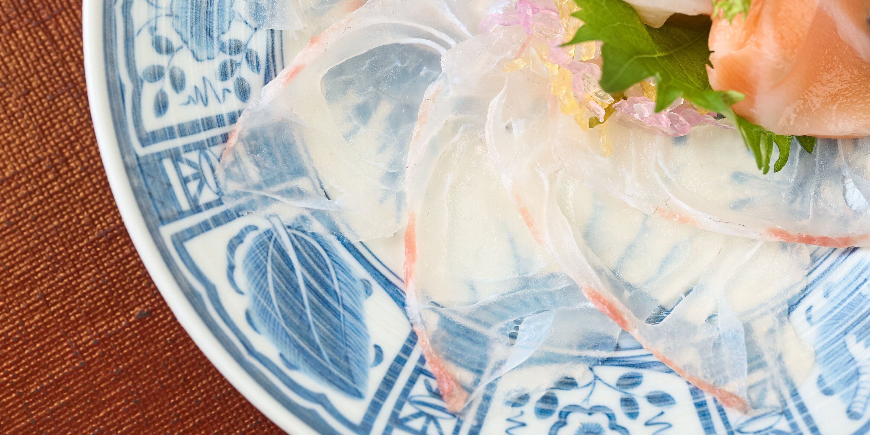 A plate with a clear gelatinous substance, possibly a dessert or dish, with a pinkish hue and some green leafy garnish.