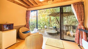 Techo de madera, un ventanal con cortinas, una mesita pequeña y una silla de mimbre.