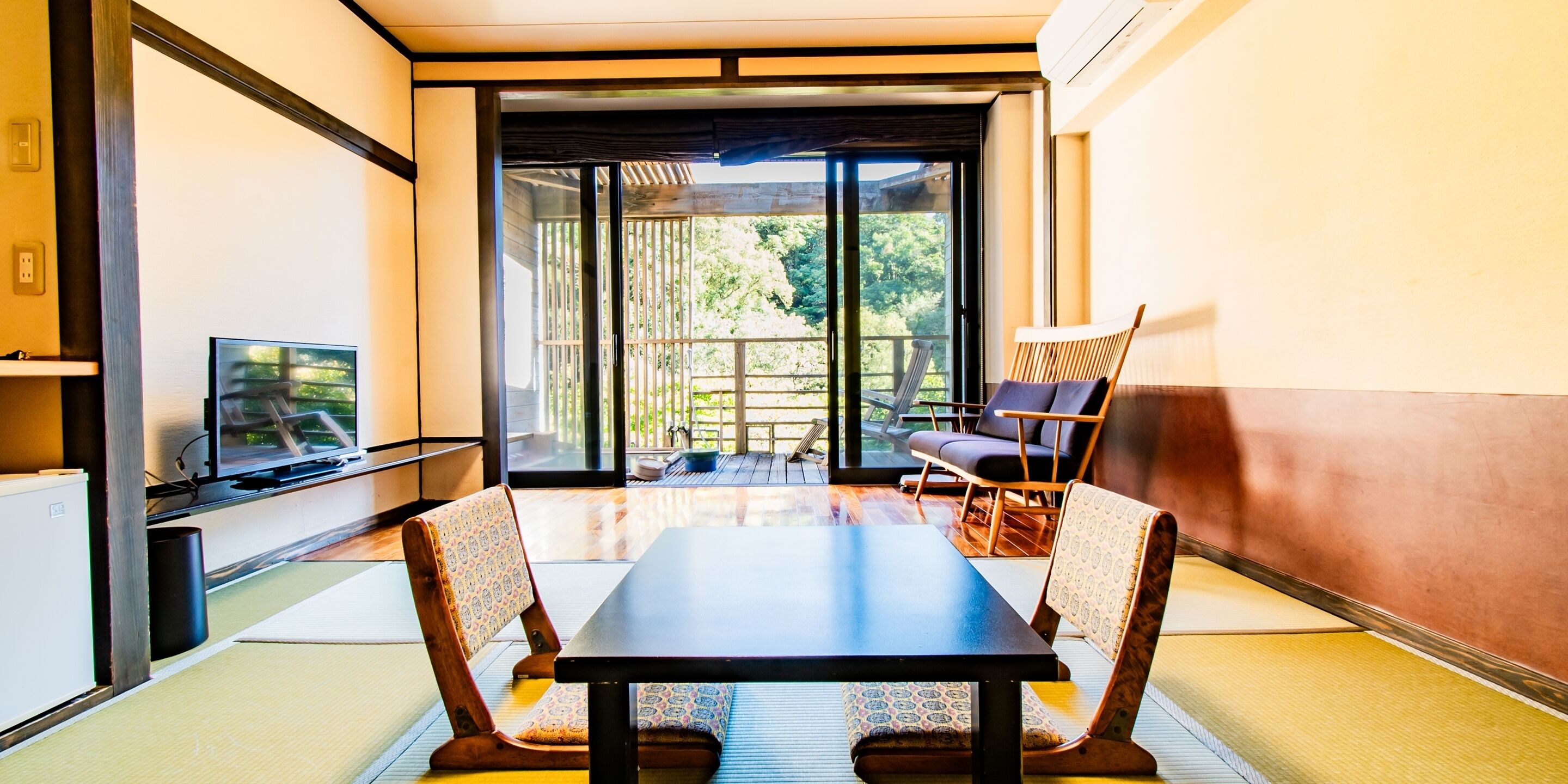 Habitación moderna con puerta de vidrio corredera que da a un balcón, una mesa con sillas y un televisor sobre un mueble.