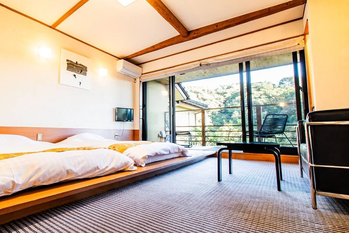 Une chambre avec deux lits, une télévision et un balcon équipé d’une chaise.