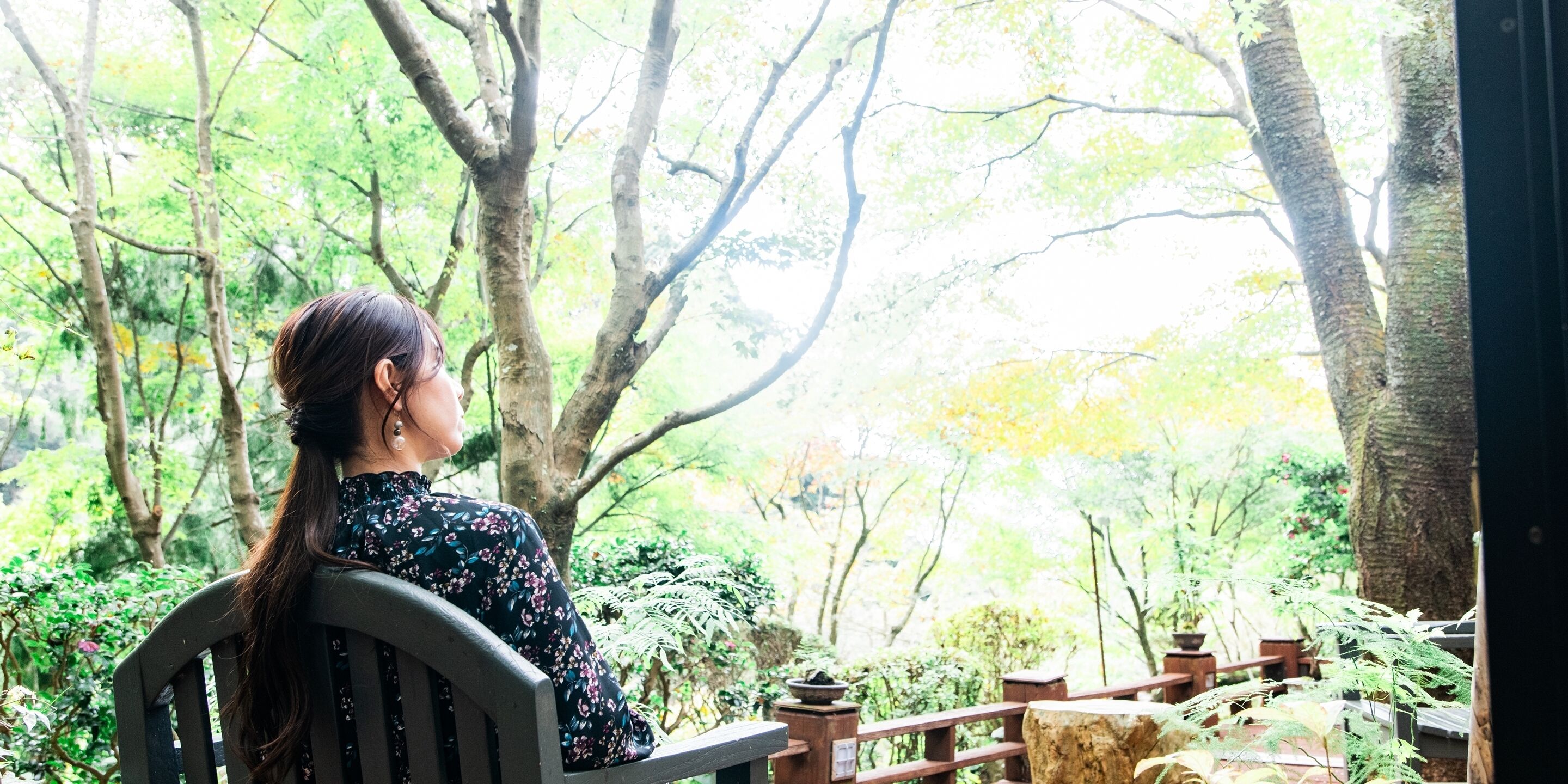 A person sitting on a wooden bench in a garden with trees and plants.