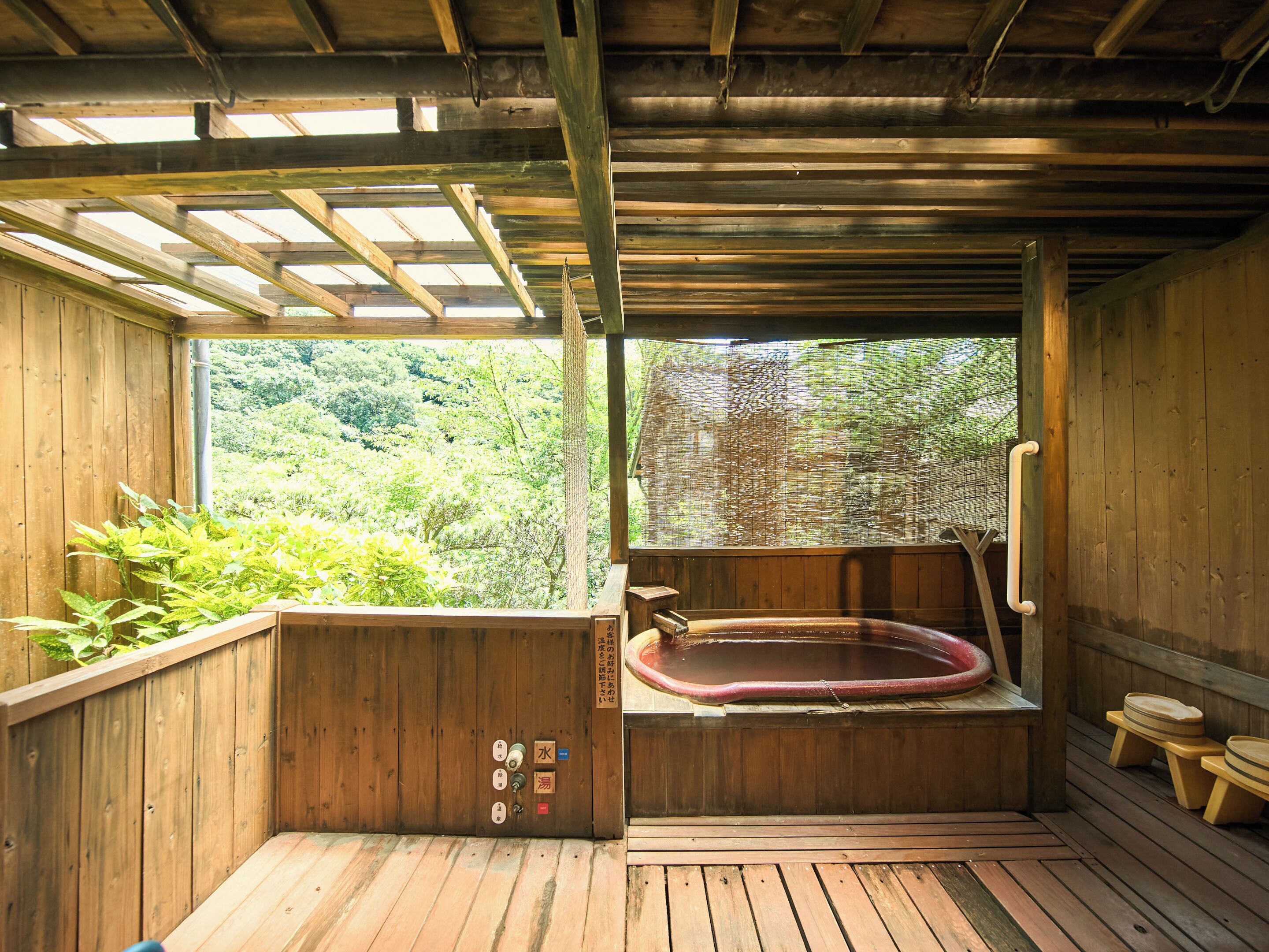A wooden hot tub with a wooden deck, a wooden bench, and a view of greenery through a window.