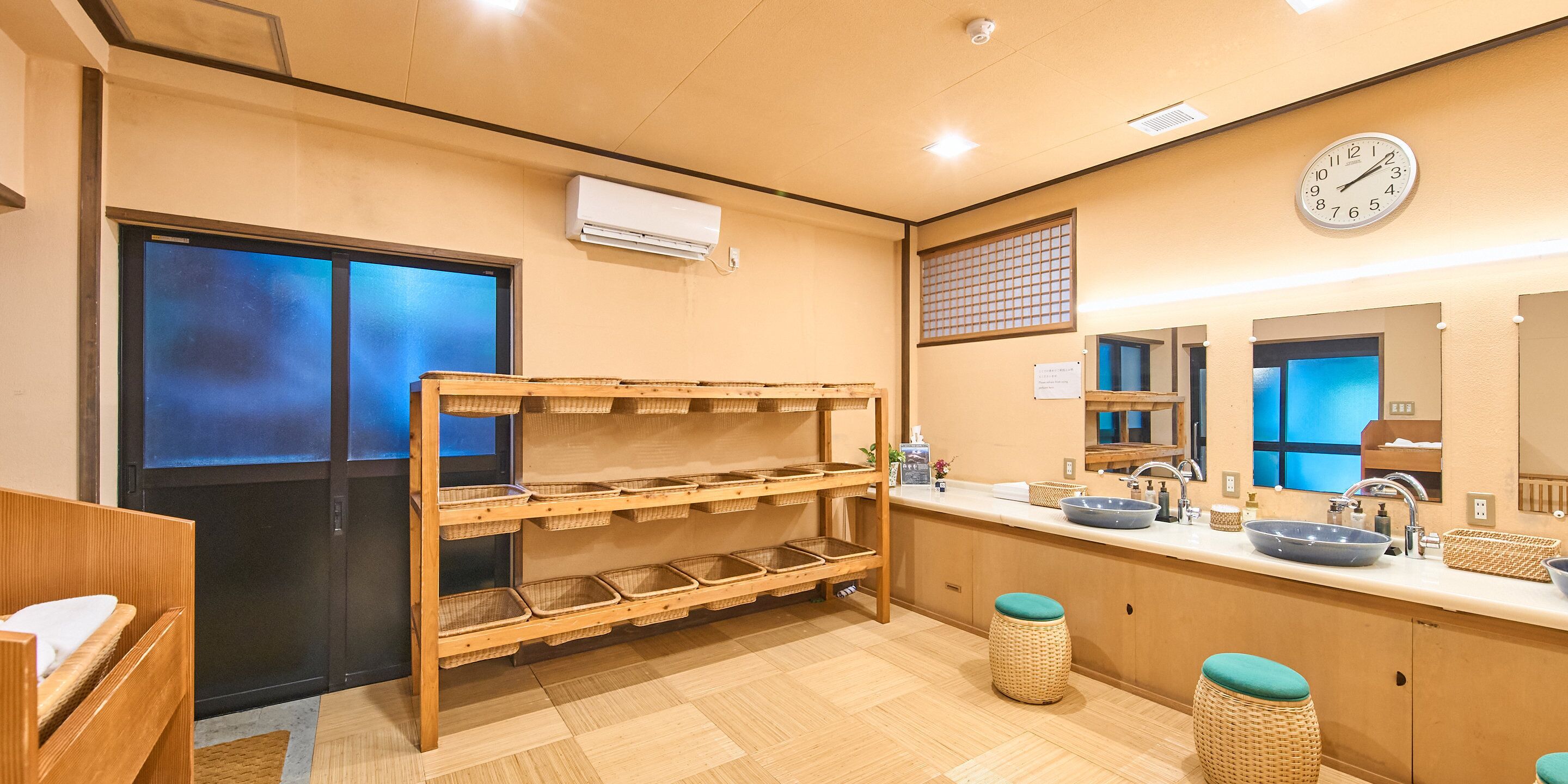 A hotel bathroom with a wooden bench, a sink with a blue basin, and a clock on the wall.