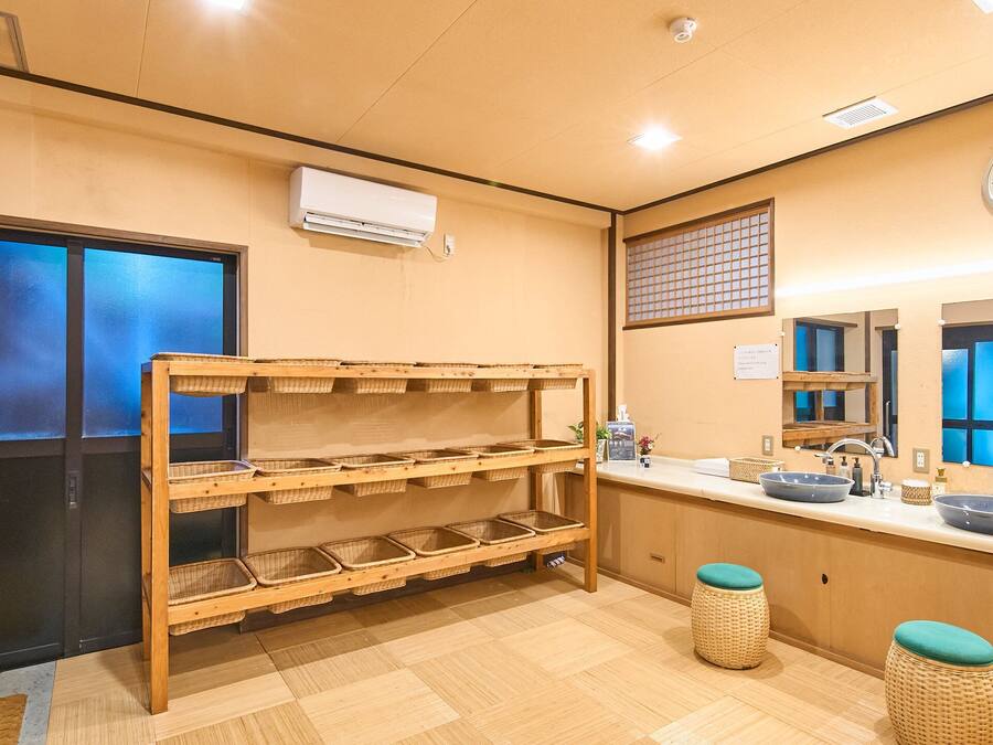 A hotel bathroom with a wooden bench, a sink with a blue basin, and a clock on the wall.