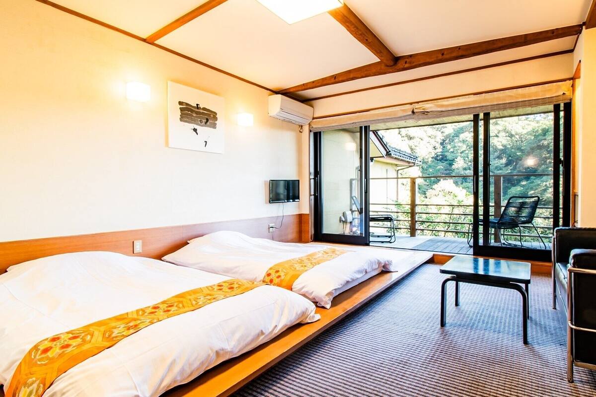 Une chambre avec deux lits, une télévision, une table et une vue sur l’extérieur.