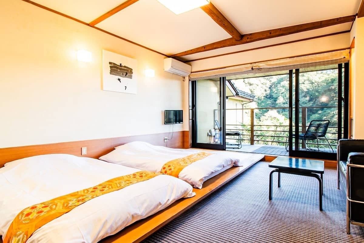 Una habitación con dos camas, televisor, una mesa y vistas al exterior.