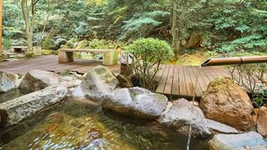 Una terraza de madera con un banco de piedra, una cascada pequeña y un arroyo rocoso.