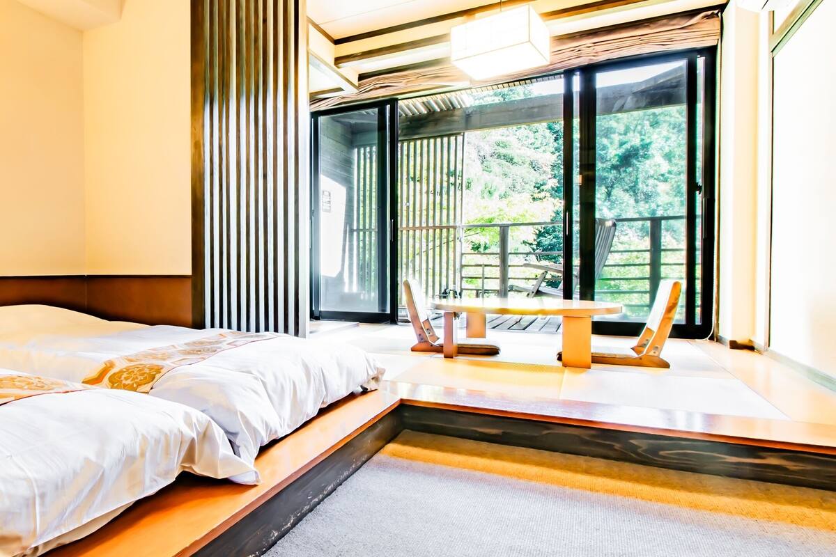 Une chambre d’hôtel avec deux lits, une petite table et une vue sur la verdure environnante.
