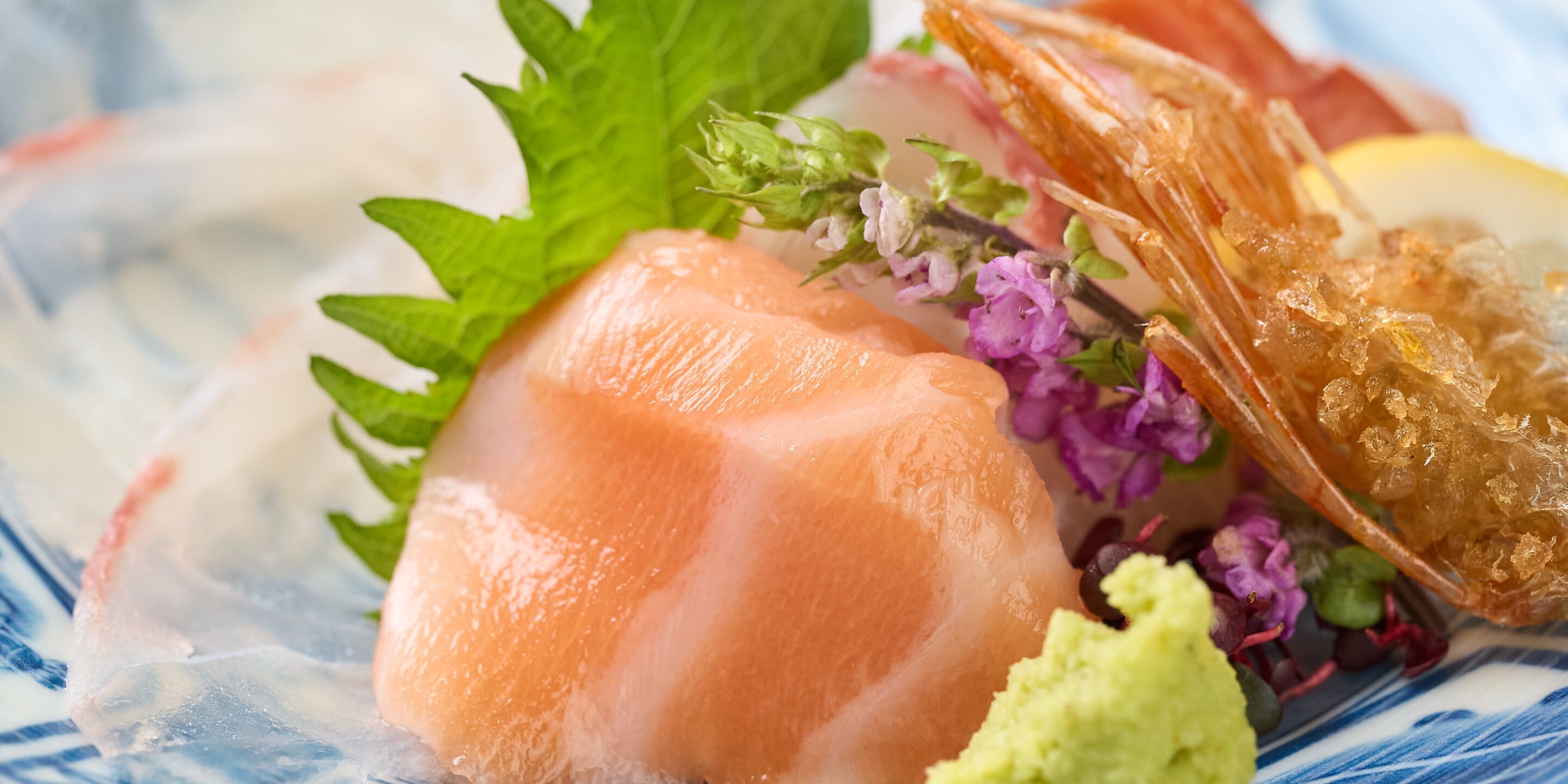 A dish with sashimi, a piece of fried seafood, and a lemon wedge.