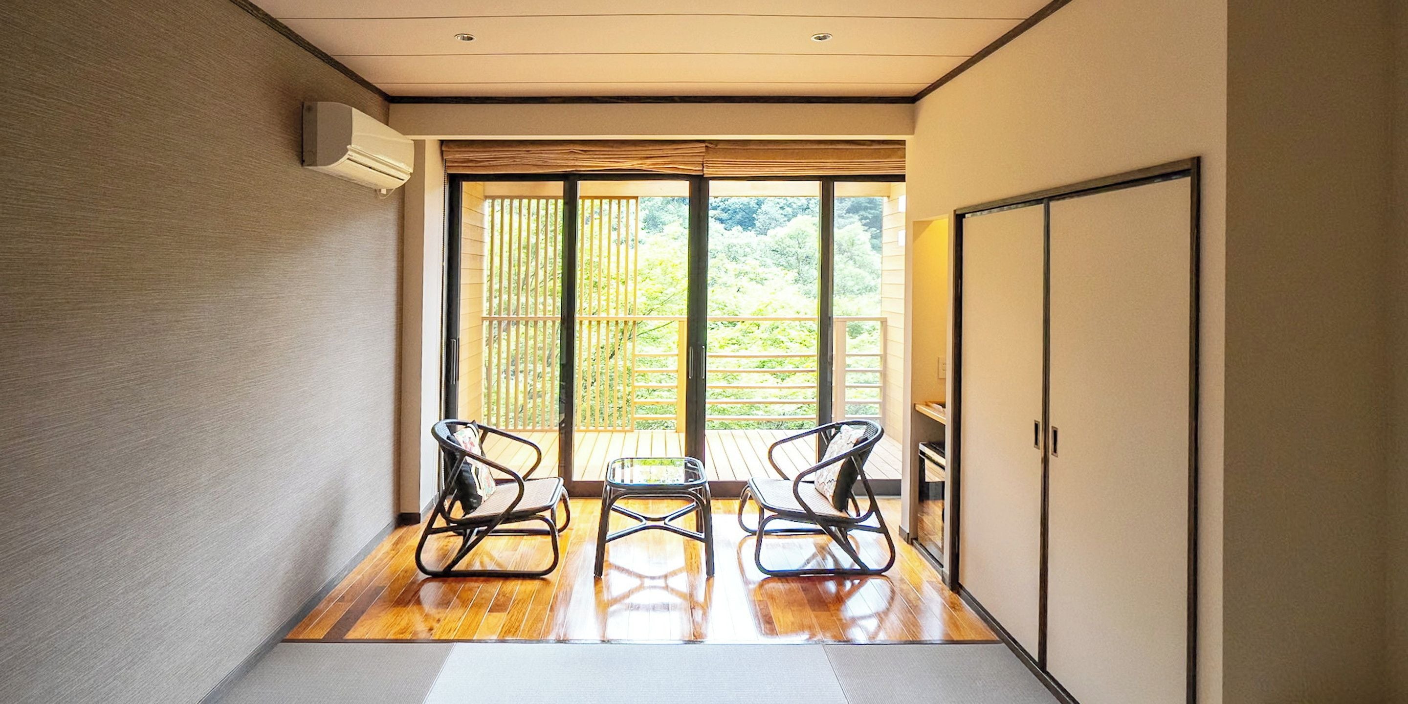 A hallway with a wooden floor, two rocking chairs, a sliding glass door leading to a balcony, and a wardrobe.