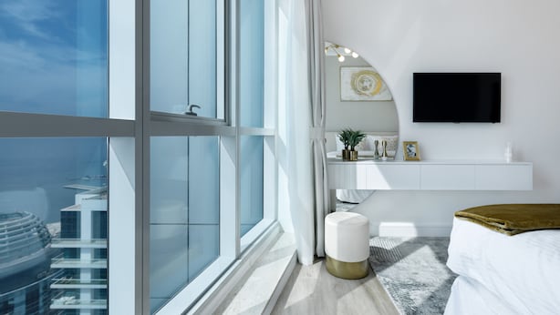 Ein modernes Schlafzimmer mit großem Fenster, einem Flachbildfernseher, einem Nachttisch und einem Bett mit goldener Tagesdecke.