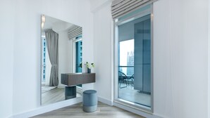 Ein modernes Hotelzimmer mit einem großen Spiegel, Holzboden, einem grauen Pouf und Blick auf die Stadt durch große Fenster.