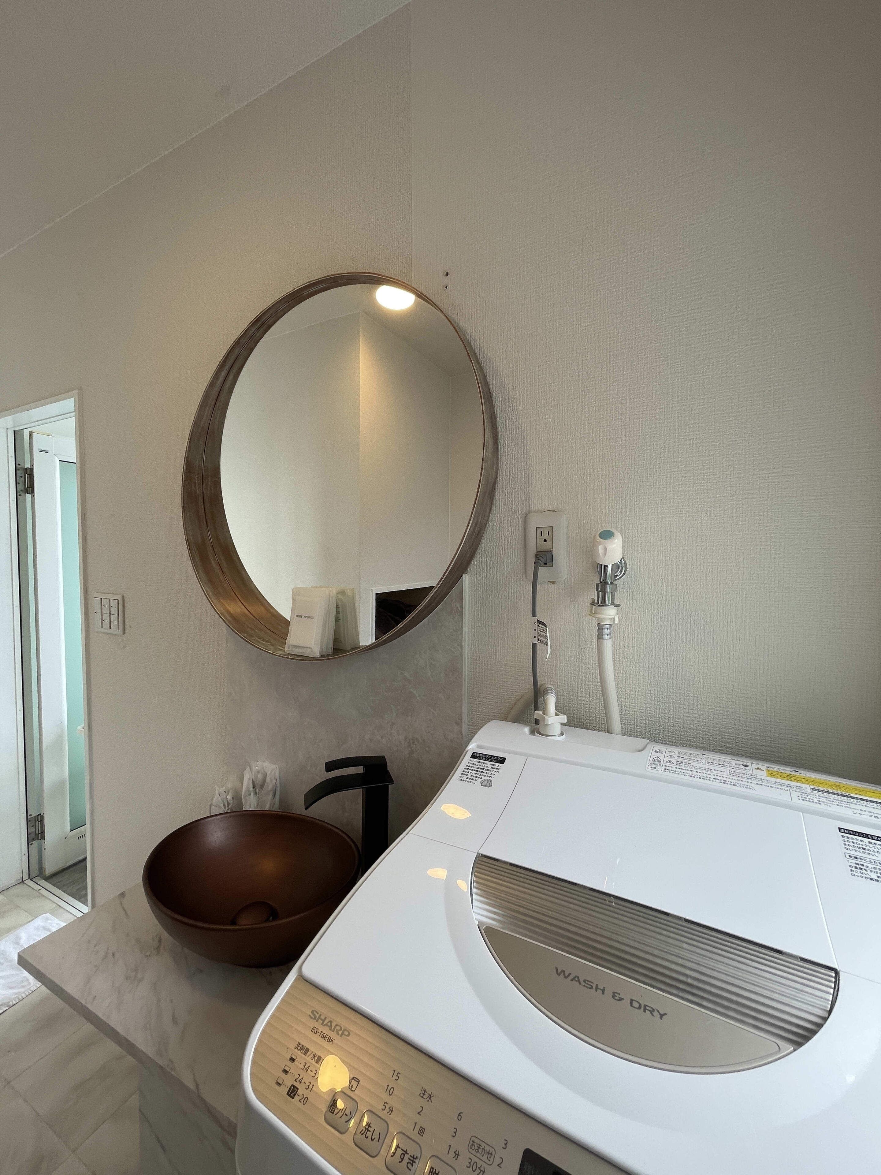 Un baño con un espejo redondo, una lavadora blanca y un tazón marrón.