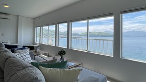 Una sala de estar moderna con un sofá grande, una mesa de centro y vista al mar a través de amplios ventanales.