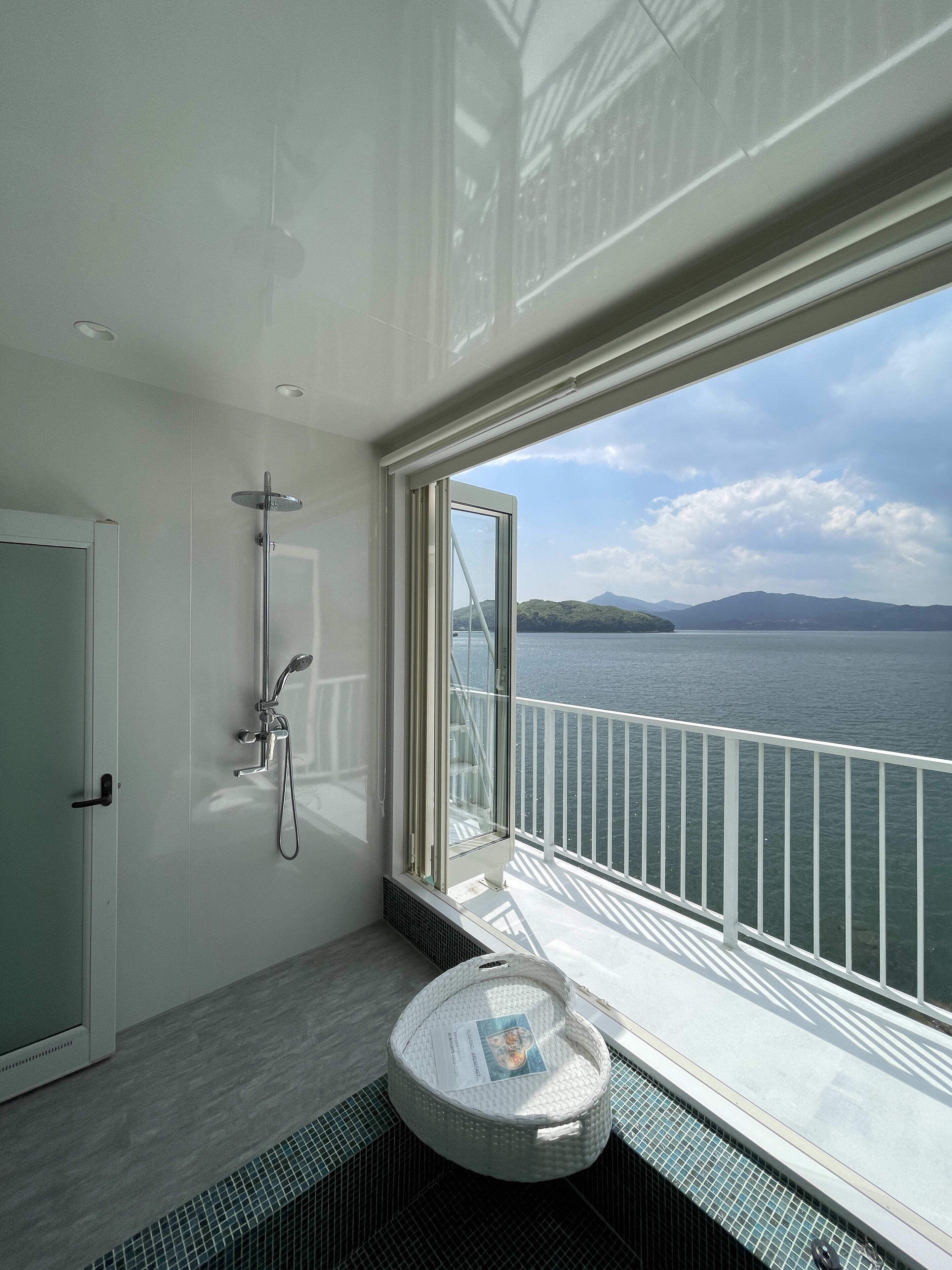 Un baño con ducha, inodoro y ventana con vistas al agua.