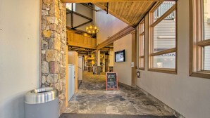 A stone-walled corridor with a welcome sign, a trash can, and a view of a mountain through large windows. - Snug Wintergreen Resort Studio: Ski In & Out! (Wintergreen Resort)