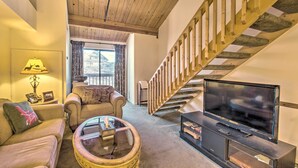 A cozy living room with a wooden staircase, a sofa, a coffee table, and a television. - Snug Wintergreen Resort Studio: Ski In & Out! (Wintergreen Resort)