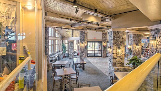 A spacious indoor area with stone walls, wooden tables, and chairs, featuring a staircase and a view of the outside. - Snug Wintergreen Resort Studio: Ski In & Out! (Wintergreen Resort)