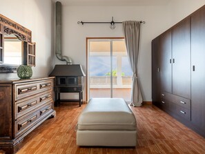 Une chambre avec une commode en bois, un banc, une armoire et une vue à travers une porte vitrée.
