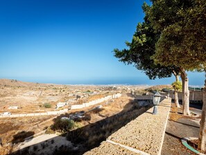 A coastal landscape with a clear sky, a paved walkway, and a view of the sea.