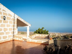 A terrace with a stone wall, a potted plant, and a view of the landscape.