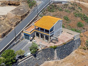 A two-story building with a tiled roof, situated on a rocky hillside with a paved road in the foreground.