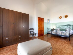 A bedroom with a large wardrobe, a bed with a metal frame, a chair, and a small table.