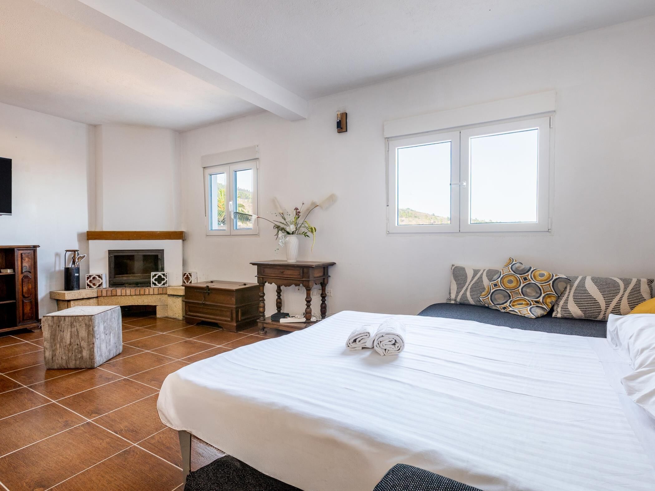 A bedroom with a bed, a bedside table, a dresser, a fireplace, and two windows.