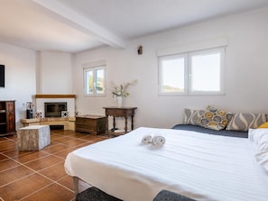 A bedroom with a bed, a bedside table, a dresser, a fireplace, and two windows.