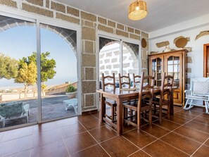 A dining area with a table and chairs, a view through a glass door, and a stone wall.