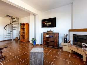 A spacious living room with a fireplace, a television mounted on the wall, and a spiral staircase leading to an upper level.