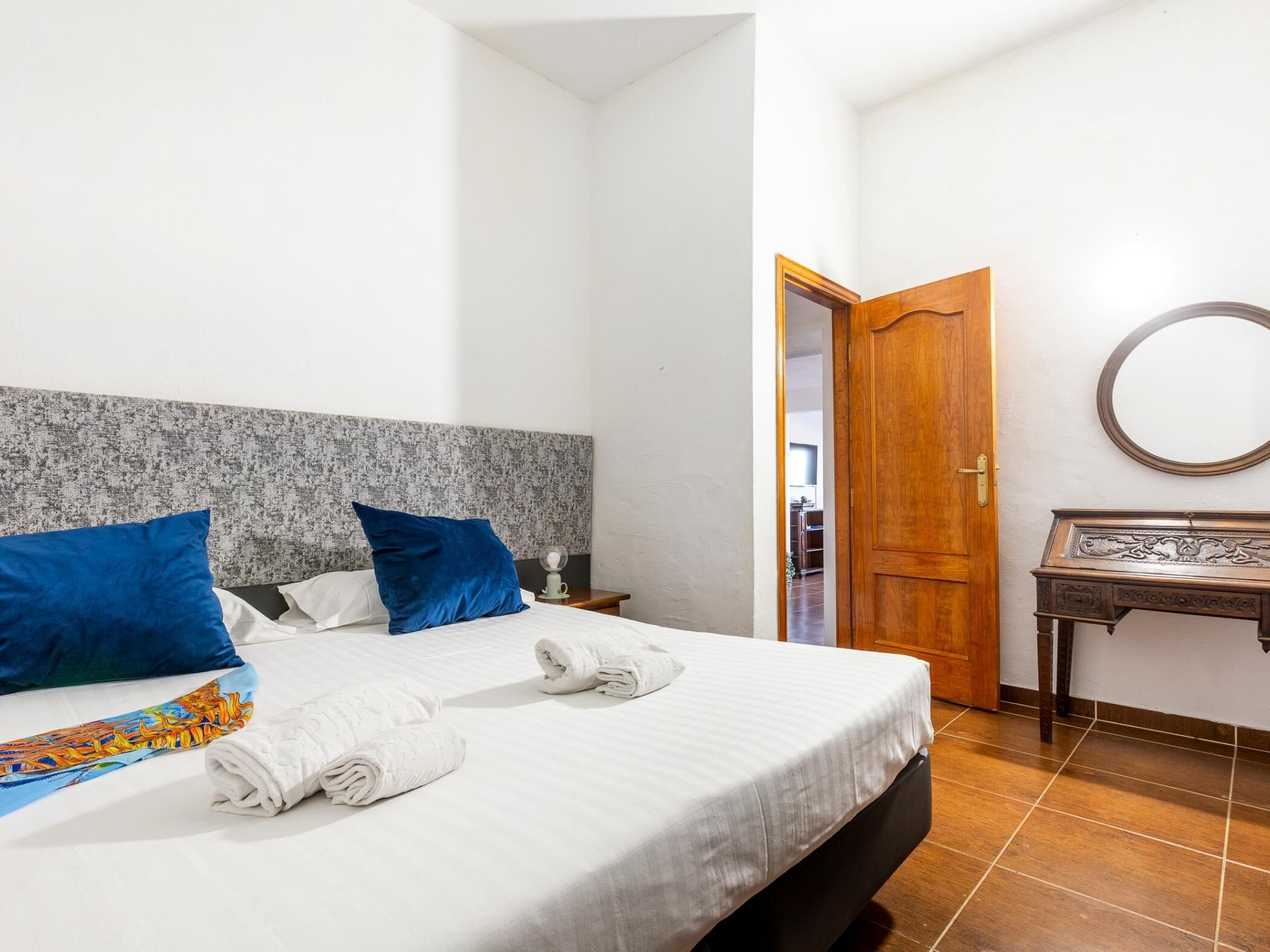 A hotel room with a bed, a wooden door, a small table, and a mirror.