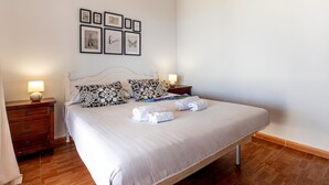 A neatly made bed with a white comforter and two pillows, a bedside table with a lamp, and a wall with framed pictures. - Finca Los Blanquitos Amazing with 3,000 m2 of land (Granadilla de Abona)